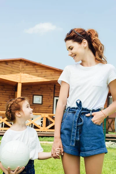 Mother and daughter with volleyball ball in white t-shirts in front of wooden cottage — Stock Photo