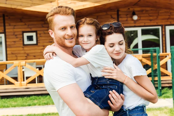 Familia joven y feliz abrazo en el jardín de casa de madera - foto de stock