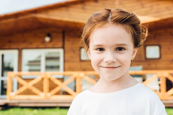 Heureux petit enfant regardant caméra en face de chalet en bois — Photo de stock