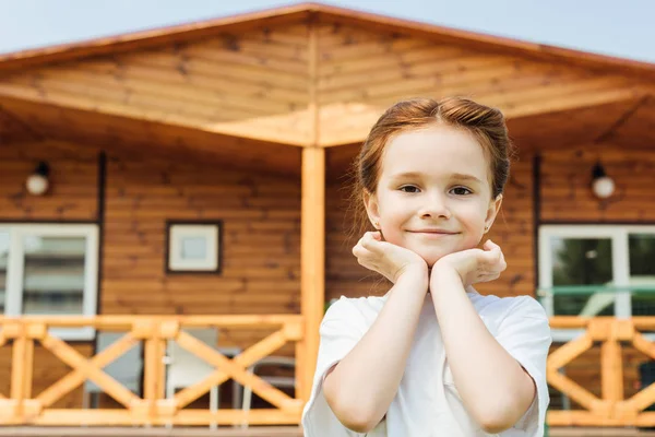 Adorable little child looking at camera in front of wooden cottage — Stock Photo