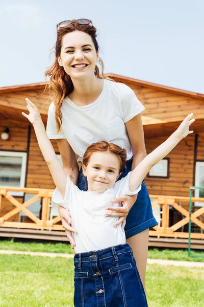 Mother and daughter in white t-shirts in front of wooden cottage — Stock Photo