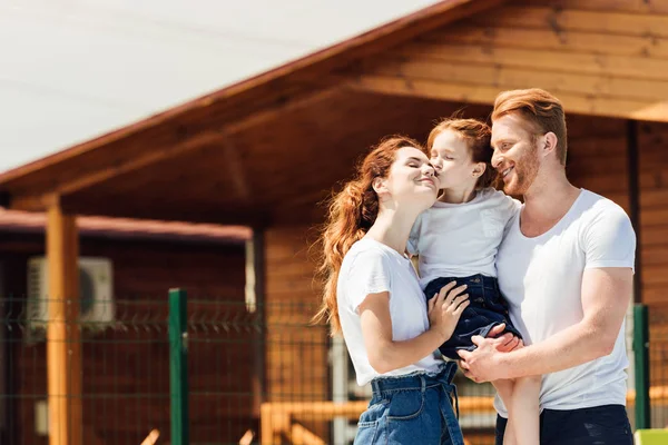 Belle jeune famille embrassant en face du chalet en bois — Photo de stock