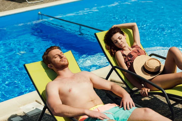 Junges Paar bräunt sich auf Liegestühlen vor Schwimmbad — Stockfoto