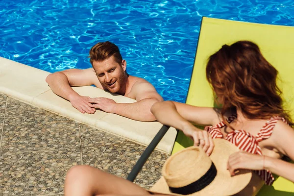 Молодой человек флиртует с женщиной, лежащей на шезлонге во время плавания в бассейне — стоковое фото
