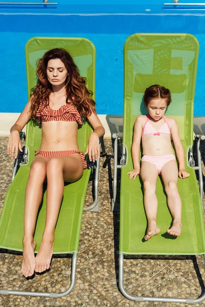 Beautiful young mother and daughter relaxing on sun loungers on poolside — Stock Photo