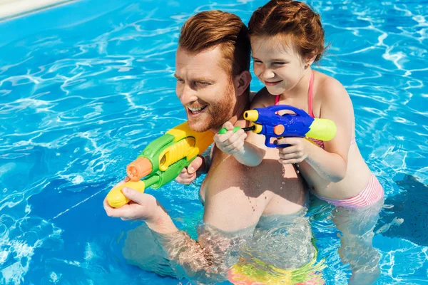 Красивый отец и очаровательная дочь играют с водяными пистолетами в бассейне — стоковое фото