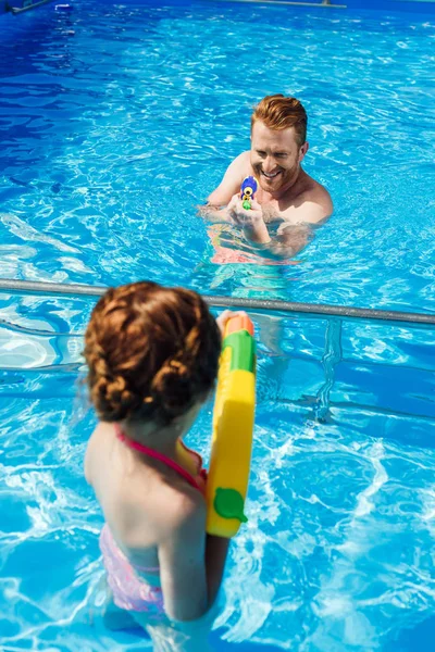Отец и маленькая дочь играют с водяными пистолетами в бассейне — стоковое фото