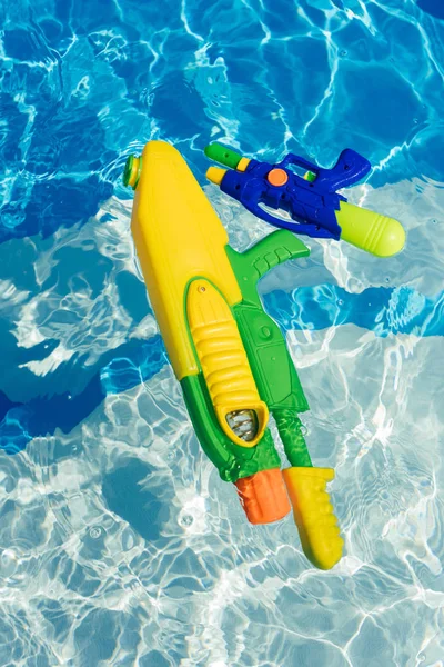 Pistolas de agua coloridas de plástico flotando en la piscina - foto de stock
