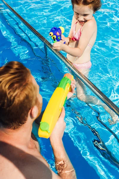 Happy father and daughter playing with water guns in swimming pool — Stock Photo