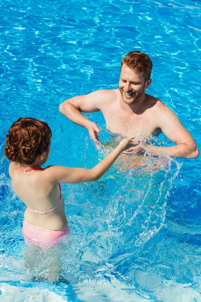 Pai feliz e filha salpicando com água na piscina — Fotografia de Stock