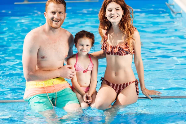 Bella giovane famiglia trascorrere del tempo in piscina e guardando la fotocamera — Foto stock