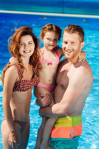Hermosa familia joven abrazándose en la piscina y mirando a la cámara - foto de stock