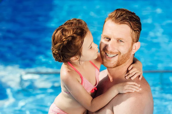 Feliz padre e hija abrazándose en la piscina y mirando a la cámara - foto de stock