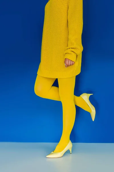 Vue recadrée de la fille en vêtements jaunes et chaussures à talons sur fond bleu — Photo de stock