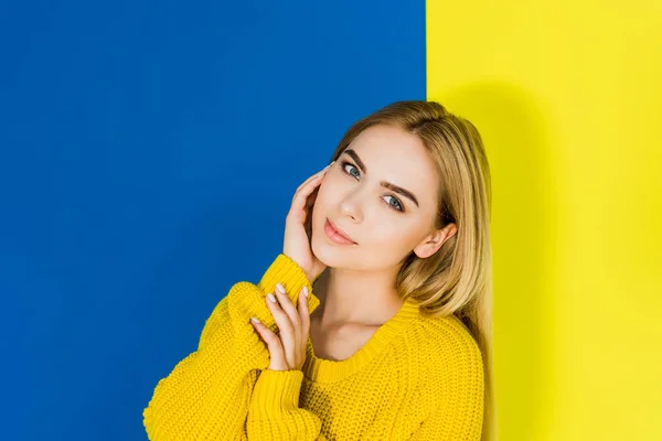 Belle fille blonde portant un pull blanc sur fond bleu et jaune — Photo de stock