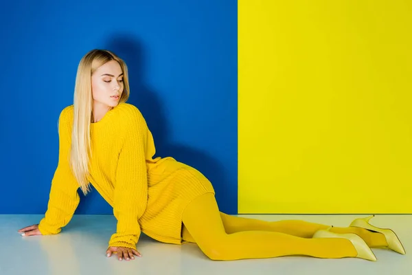 Elegant blonde woman all dressed in yellow posing on blue and yellow background — Stock Photo
