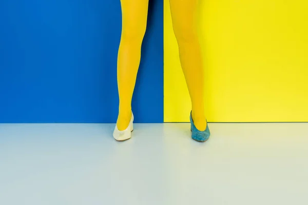 Cropped view of female legs in different shoes on blue and yellow background — Stock Photo