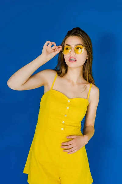 Attractive young girl wearing yellow sunglasses posing on blue background — Stock Photo