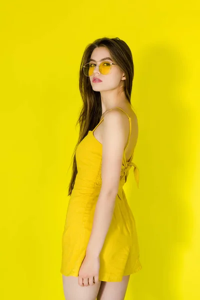 Model in gelbem Kleid und Sonnenbrille posiert auf gelbem Hintergrund — Stockfoto