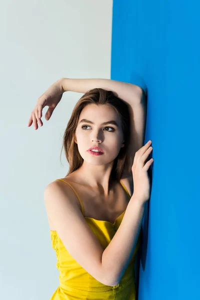 Elegant brunette woman standing by blue and yellow background — Stock Photo