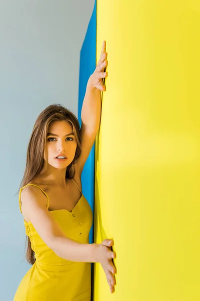 Beautiful brunette girl standing by blue and yellow background — Stock Photo