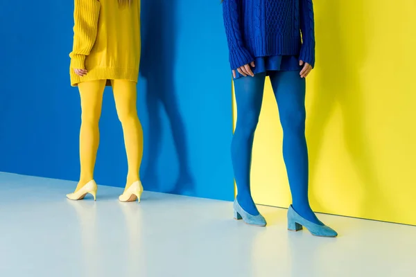 Cropped view of women in contrasting clothes standing back to back on blue and yellow background — Stock Photo