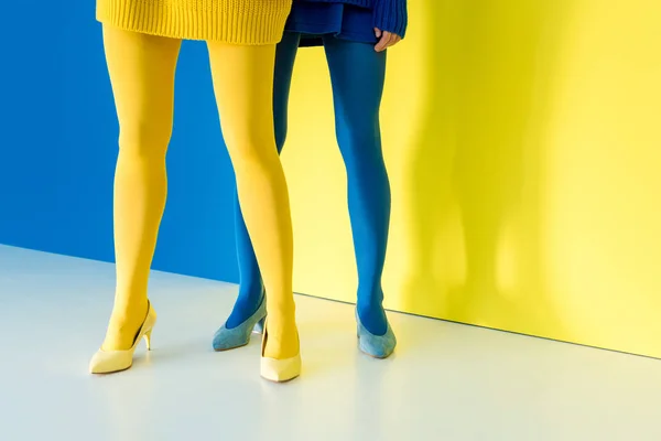 Vista recortada de las piernas femeninas en pantimedias azules y amarillas sobre fondo azul y amarillo - foto de stock