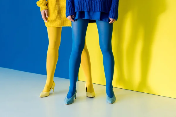 Vista recortada de las mujeres que usan pantimedias azules y amarillas sobre fondo azul y amarillo - foto de stock