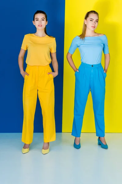 Chicas jóvenes atractivas en trajes azules y amarillos posando sobre fondo azul y amarillo - foto de stock