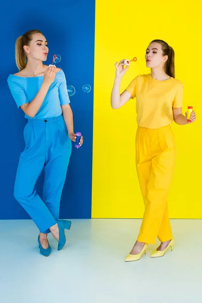 Chicas alegres soplando burbujas sobre fondo azul y amarillo - foto de stock