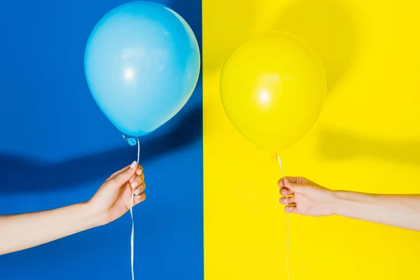 Vista recortada de las manos de las mujeres con globos sobre fondo azul y amarillo - foto de stock