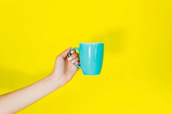 Vue recadrée de la main féminine avec tasse bleue sur fond jaune — Photo de stock
