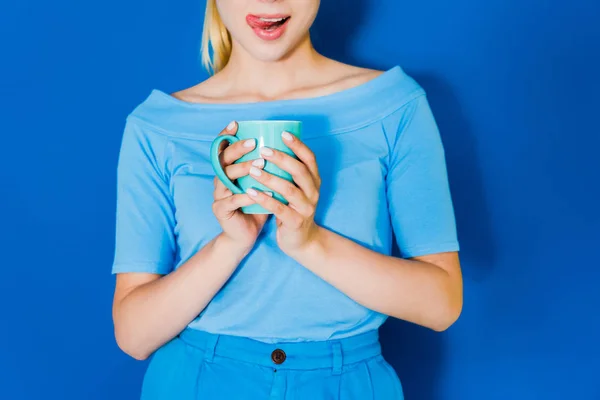 Attraktives junges Mädchen in blauer Kleidung mit blauer Tasse in der Hand auf blauem Hintergrund — Stockfoto