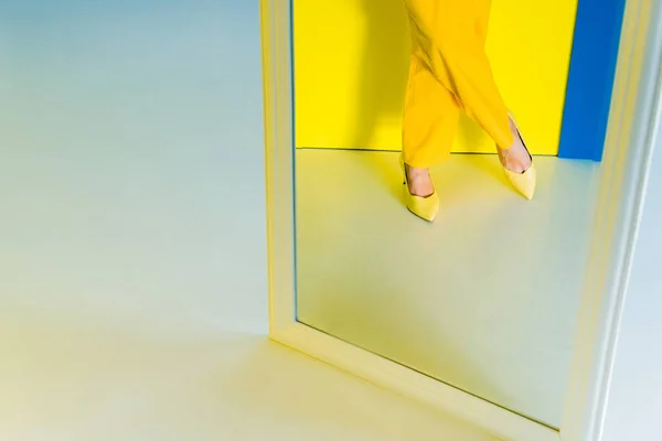 Vista del espejo recortado de la mujer con zapatos amarillos sobre fondo azul y amarillo - foto de stock