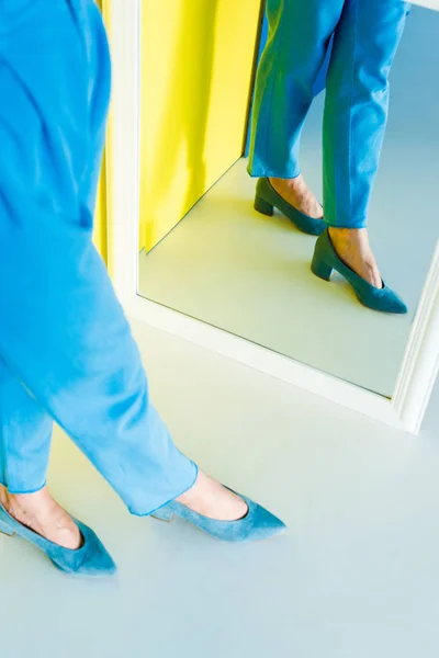 Cropped mirror view of woman in blue clothes and shoes on blue and yellow background — Stock Photo