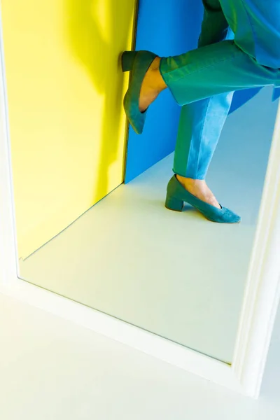 Cropped view of female feet in blue heeled shoes on blue and yellow background — Stock Photo