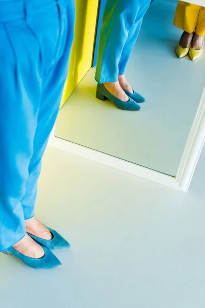 Обрезанный вид женщин, позирующих с помощью зеркала на синем и желтом фоне — стоковое фото