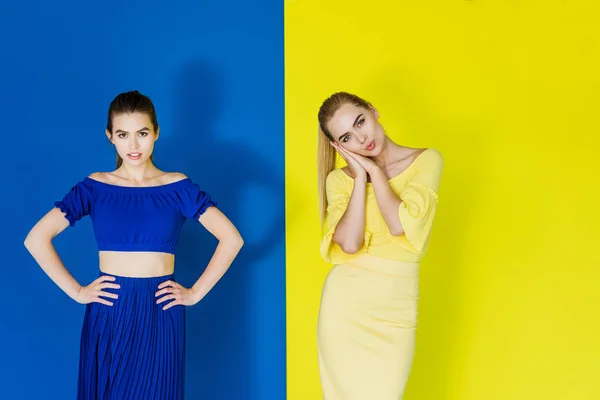 Attractive young girls in blue and yellow outfits posing on matching backgrounds — Stock Photo