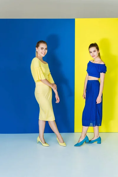 Modelos de moda femenina en trajes azules y amarillos posando sobre fondos a juego - foto de stock