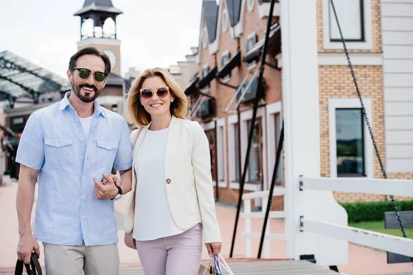 Sonriente pareja cogida de la mano y mirando a la cámara en la calle - foto de stock