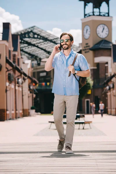 Hombre guapo hablando por teléfono inteligente y caminando en la calle - foto de stock