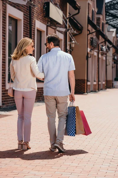 Visão traseira do casal andando com sacos de compras na rua — Fotografia de Stock