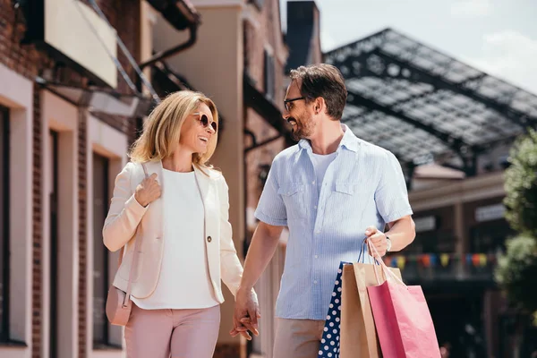 Affectionate couple holding hands and walking with shopping bags on street — Stock Photo