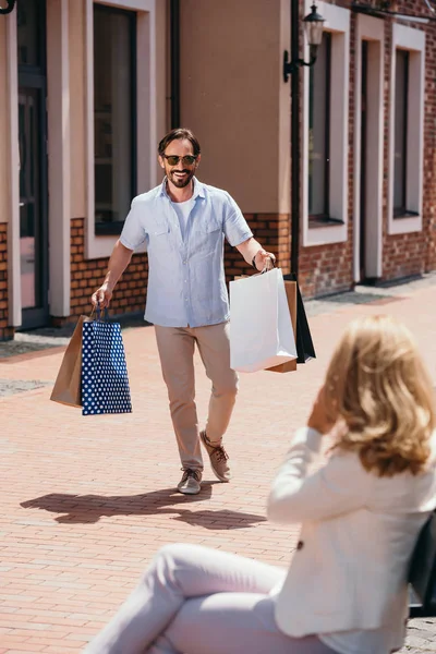 Mujer sentada en el banco y hombre caminando con bolsas de compras - foto de stock