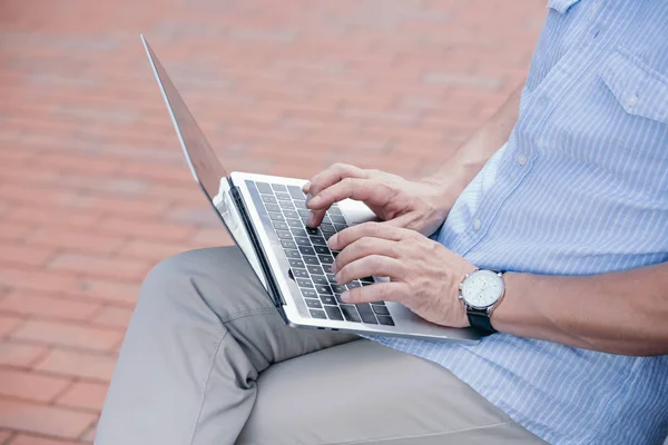 Обрезанное изображение человека, сидящего на скамейке с ноутбуком — стоковое фото