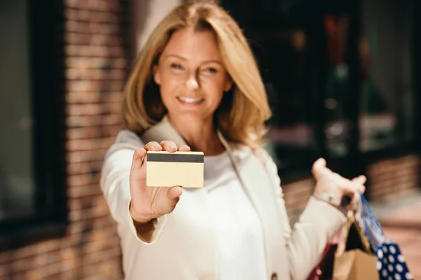 Donna attraente mostrando carta di credito e tenendo borse della spesa sulla strada — Foto stock