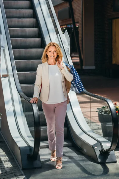 Beautiful woman standing near escalator with shopping bags in mall — Stock Photo