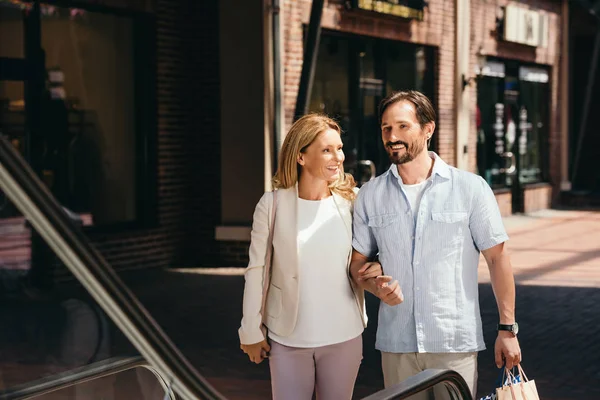 Happy couple stepping on escalator in shopping mall — Stock Photo