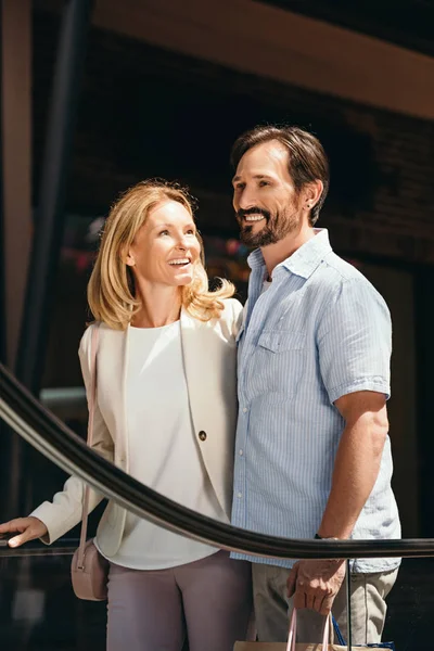 Smiling couple on moving staircase in shopping mall — Stock Photo