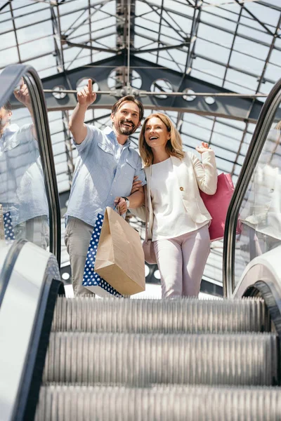 Low angle view of couple looking at something in shopping mall from escalator — Stock Photo